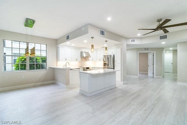 kitchen featuring appliances with stainless steel finishes, white cabinetry, wall chimney range hood, light hardwood / wood-style floors, and hanging light fixtures