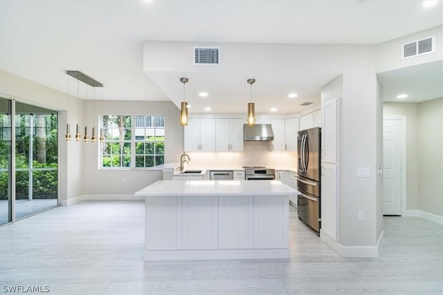 kitchen featuring white cabinetry, stainless steel appliances, wall chimney range hood, pendant lighting, and sink