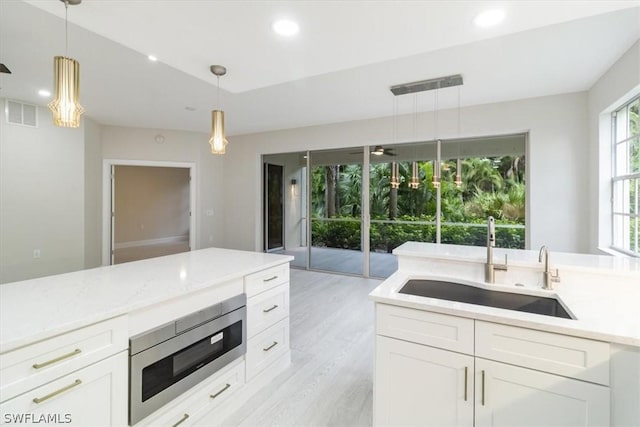 kitchen with white cabinets, decorative light fixtures, light hardwood / wood-style floors, sink, and stainless steel microwave