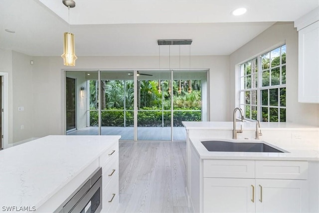 kitchen featuring white cabinets, sink, hanging light fixtures, light stone counters, and light hardwood / wood-style flooring