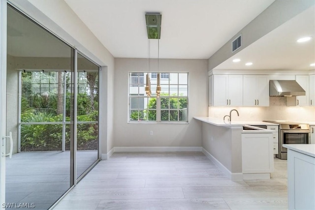 kitchen featuring white cabinets, wall chimney range hood, backsplash, stainless steel electric range oven, and a notable chandelier