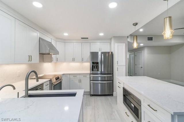 kitchen with white cabinetry, appliances with stainless steel finishes, tasteful backsplash, wall chimney range hood, and pendant lighting