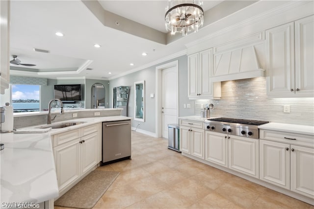 kitchen with ceiling fan with notable chandelier, a raised ceiling, custom exhaust hood, appliances with stainless steel finishes, and sink