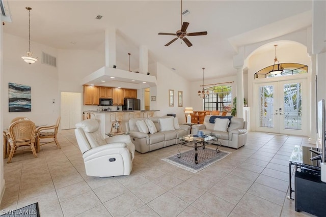 tiled living room featuring a high ceiling, ceiling fan with notable chandelier, decorative columns, and french doors