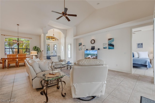 living room with french doors, ornate columns, light tile flooring, ceiling fan with notable chandelier, and high vaulted ceiling