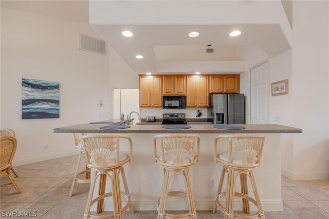 kitchen featuring appliances with stainless steel finishes, a kitchen island with sink, a breakfast bar area, sink, and light tile floors