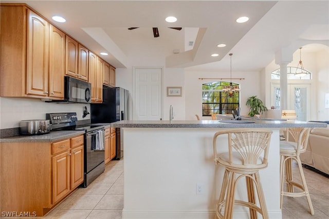 kitchen with hanging light fixtures, light tile patterned floors, a kitchen breakfast bar, an island with sink, and black appliances