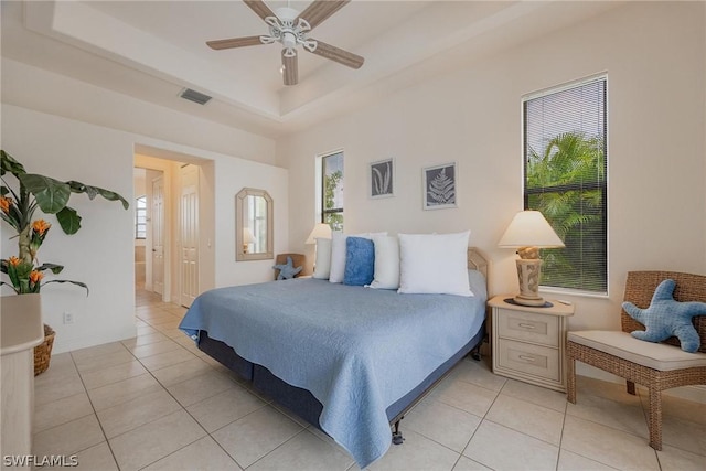 bedroom with light tile patterned flooring, ceiling fan, and a tray ceiling