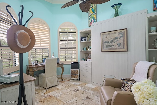 home office with built in shelves, baseboards, ceiling fan, and stone tile flooring