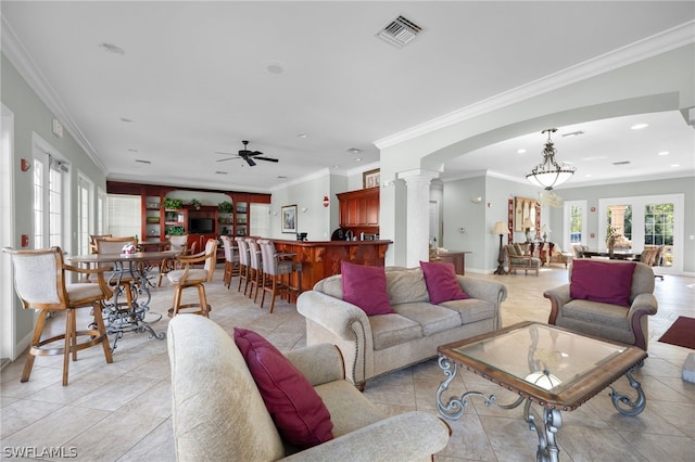 tiled living room with decorative columns, ceiling fan with notable chandelier, and ornamental molding