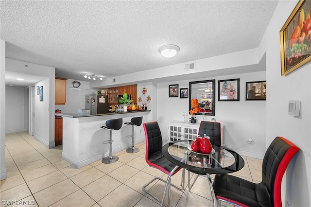 interior space with a breakfast bar area, stainless steel refrigerator, light tile patterned floors, a textured ceiling, and kitchen peninsula