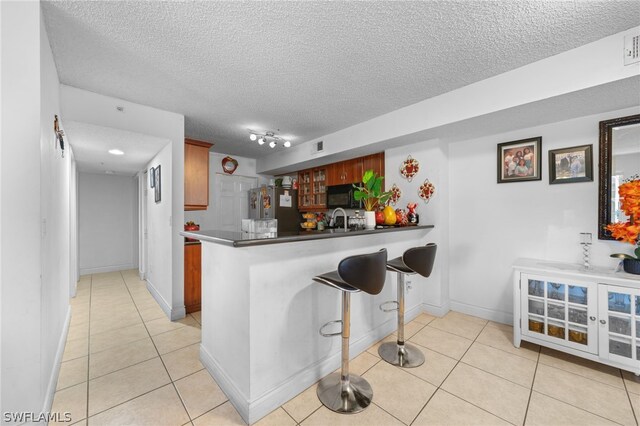 kitchen featuring light tile patterned flooring, stainless steel fridge, a textured ceiling, kitchen peninsula, and track lighting