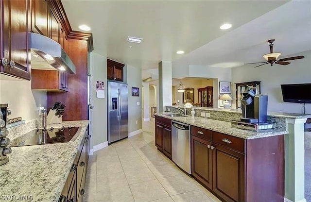 kitchen featuring stainless steel appliances, light stone counters, wall chimney exhaust hood, ceiling fan, and light tile floors