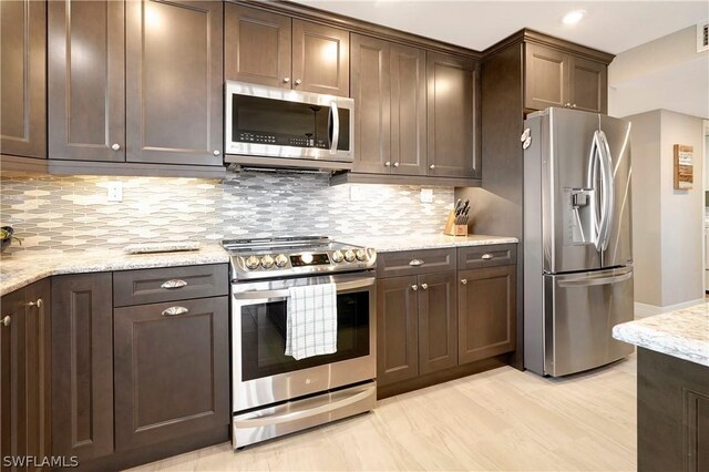 kitchen with appliances with stainless steel finishes, backsplash, dark brown cabinetry, and light stone countertops