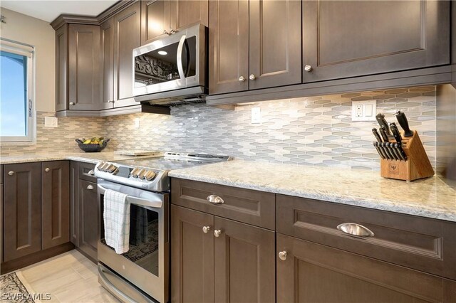 kitchen with dark brown cabinets, backsplash, stainless steel appliances, and light stone counters