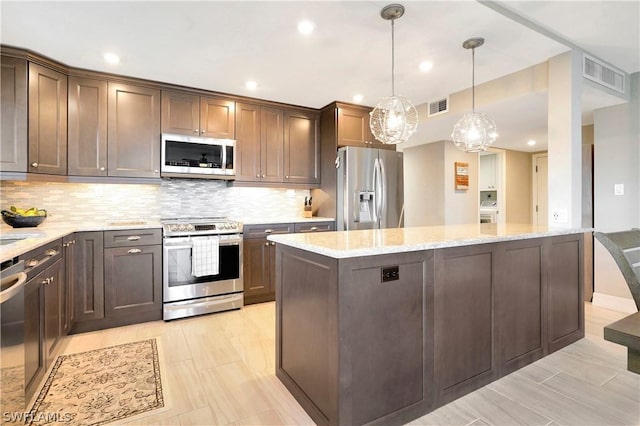 kitchen featuring stainless steel appliances, a center island, backsplash, visible vents, and light stone countertops