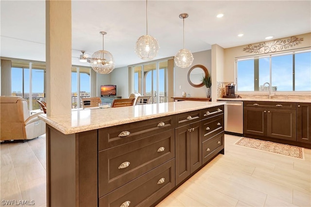 kitchen featuring a wealth of natural light, sink, light stone counters, stainless steel dishwasher, and decorative light fixtures