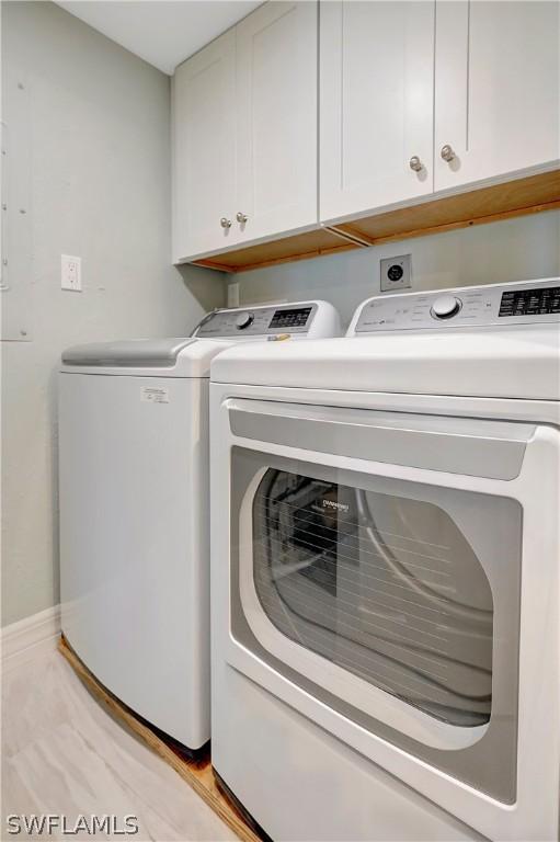 clothes washing area with washer and clothes dryer and cabinets