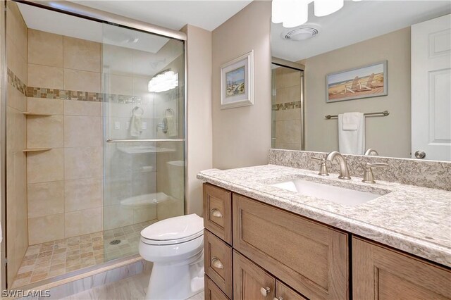 bathroom featuring a shower with door, vanity, and toilet