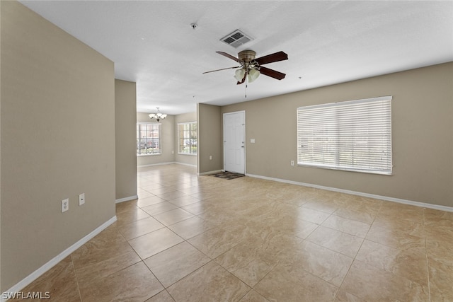 tiled empty room featuring ceiling fan with notable chandelier