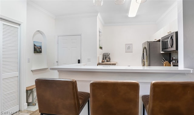 kitchen with white cabinets, crown molding, appliances with stainless steel finishes, kitchen peninsula, and a kitchen breakfast bar