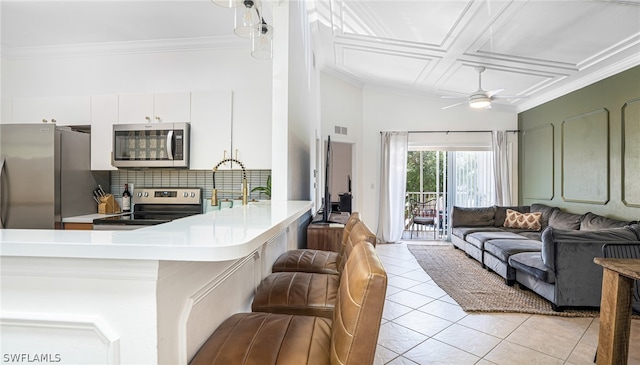 kitchen featuring white cabinetry, a breakfast bar, coffered ceiling, appliances with stainless steel finishes, and decorative backsplash