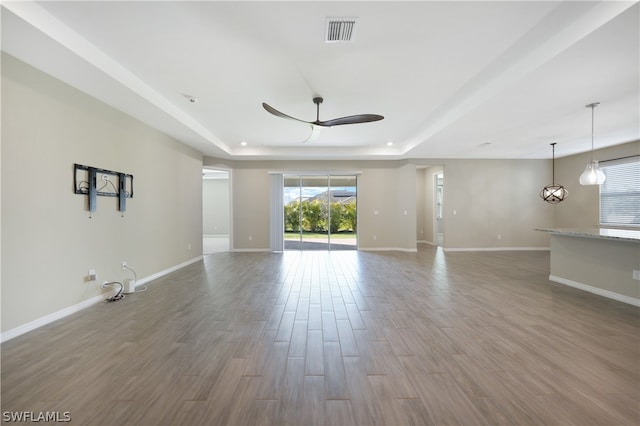 unfurnished living room with a tray ceiling, hardwood / wood-style flooring, and ceiling fan