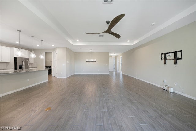 unfurnished living room with a raised ceiling, ceiling fan with notable chandelier, and hardwood / wood-style floors