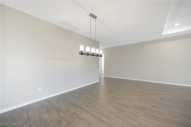 empty room with wood-type flooring and an inviting chandelier