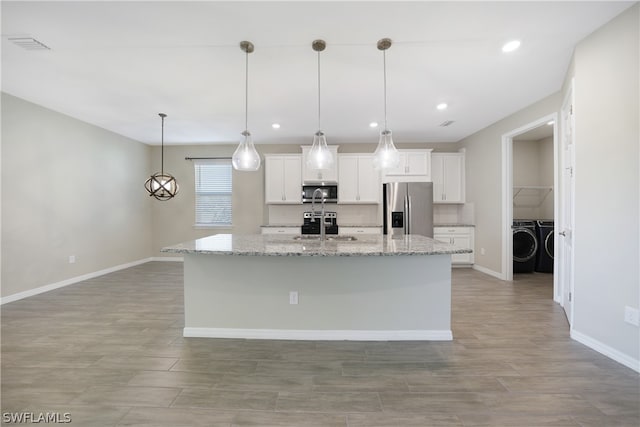 kitchen featuring a center island with sink, white cabinetry, light stone countertops, washing machine and dryer, and appliances with stainless steel finishes