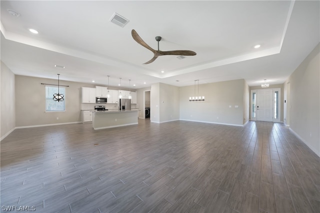 unfurnished living room featuring hardwood / wood-style flooring, a tray ceiling, and ceiling fan with notable chandelier