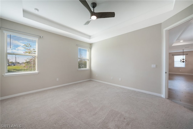 empty room featuring ceiling fan, a tray ceiling, hardwood / wood-style floors, and a wealth of natural light