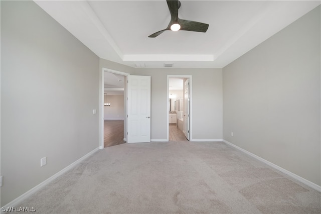 unfurnished bedroom with ceiling fan, connected bathroom, hardwood / wood-style flooring, and a tray ceiling