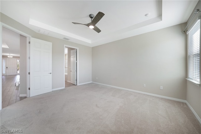 unfurnished bedroom featuring ceiling fan, carpet flooring, multiple windows, and a raised ceiling