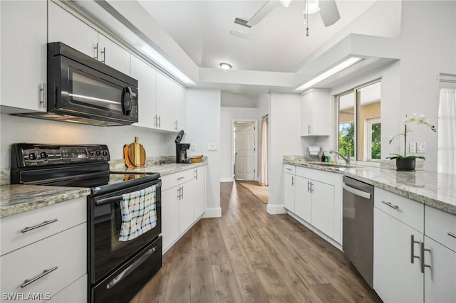 kitchen with white cabinetry, wood-type flooring, light stone countertops, black appliances, and sink