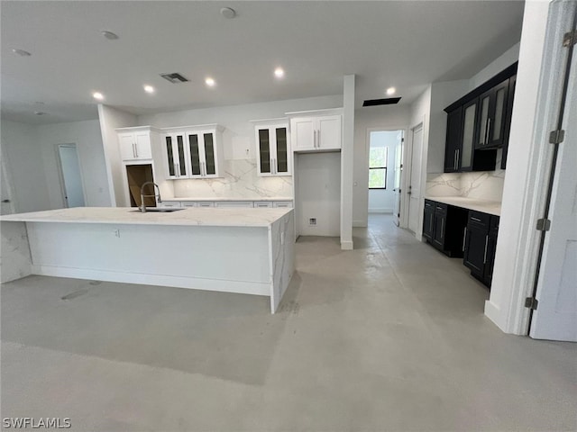 kitchen featuring decorative backsplash, light stone counters, sink, a center island with sink, and white cabinets