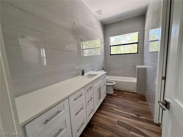 full bathroom featuring vanity, hardwood / wood-style flooring, tiled shower / bath combo, toilet, and tile walls