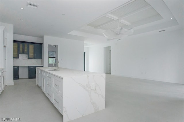 interior space featuring light stone counters, sink, white cabinetry, and an island with sink