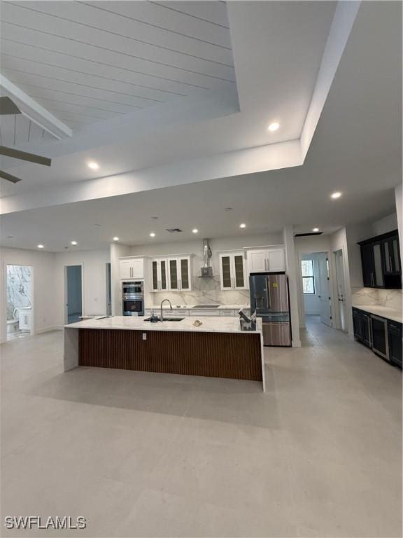 kitchen with a spacious island, wall chimney exhaust hood, appliances with stainless steel finishes, white cabinets, and backsplash