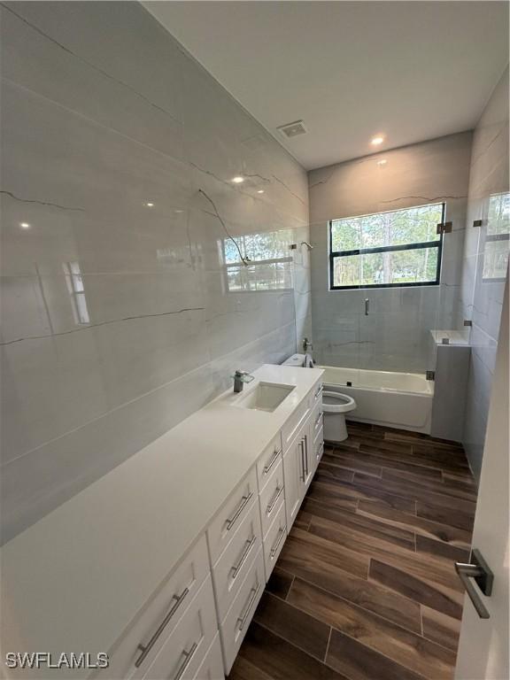 full bathroom with tiled shower / bath combo, vanity, tile walls, and toilet