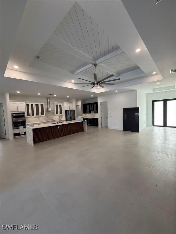 unfurnished living room with sink, ceiling fan, and a tray ceiling