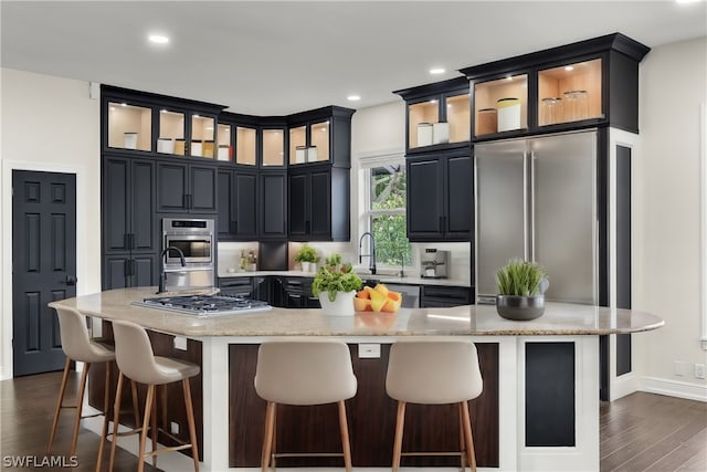 kitchen with light stone countertops, stainless steel appliances, dark hardwood / wood-style flooring, a large island with sink, and sink