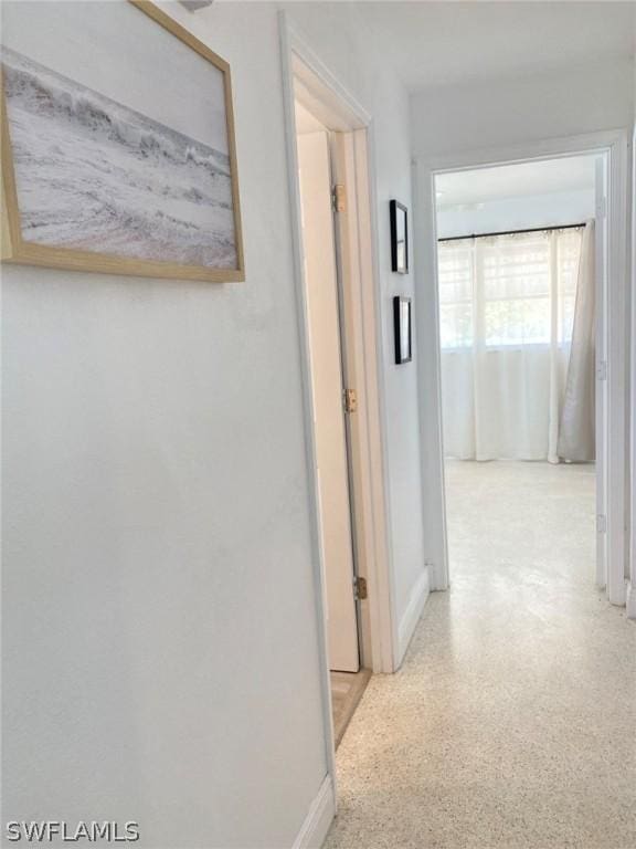 corridor featuring light speckled floor and baseboards