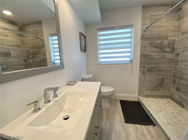 bathroom with wood finished floors, tiled shower, vanity, and toilet