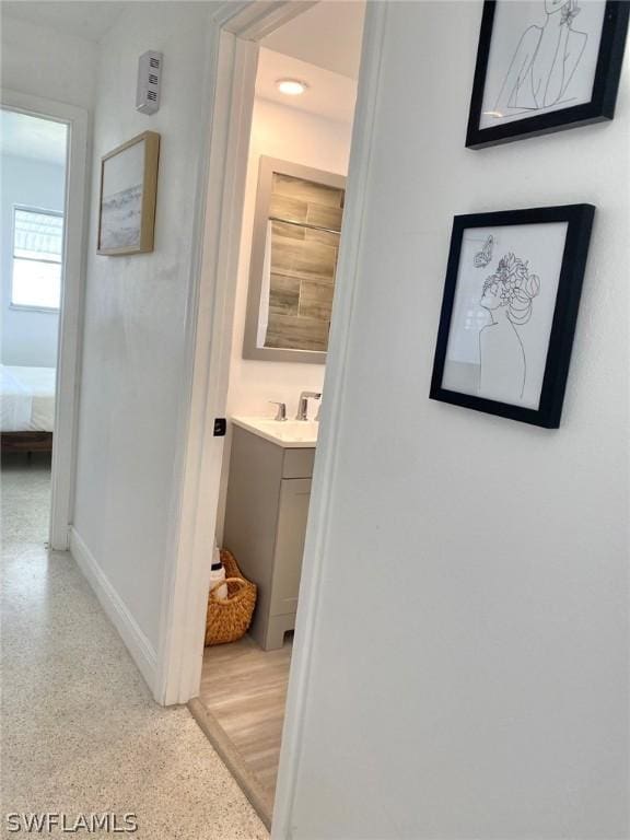 corridor featuring baseboards, light speckled floor, and a sink