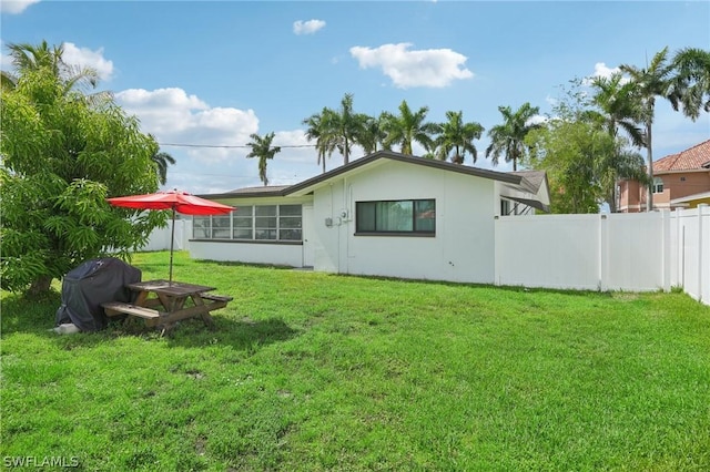 rear view of property with stucco siding, a lawn, and fence