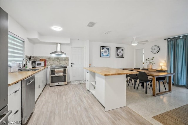 kitchen featuring visible vents, butcher block countertops, appliances with stainless steel finishes, wall chimney range hood, and open shelves