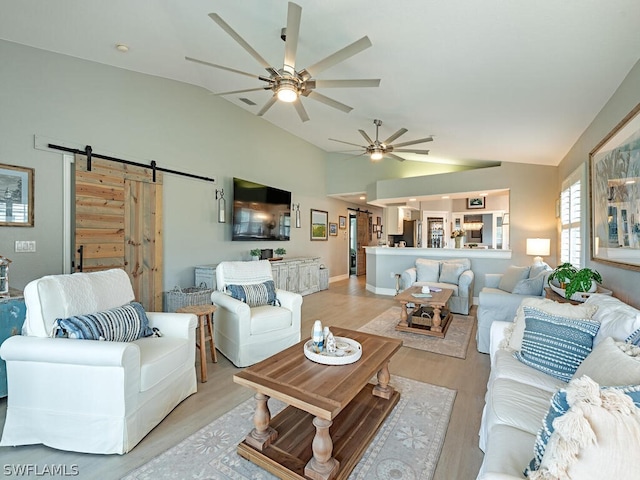 living room with vaulted ceiling, light hardwood / wood-style floors, a barn door, and ceiling fan