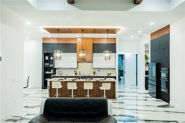 kitchen with an inviting chandelier, tasteful backsplash, pendant lighting, a kitchen island with sink, and a breakfast bar