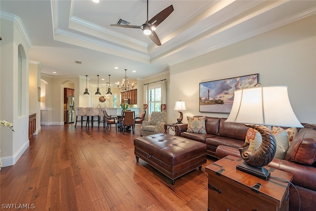 living room featuring a raised ceiling, crown molding, wood-type flooring, and ceiling fan with notable chandelier